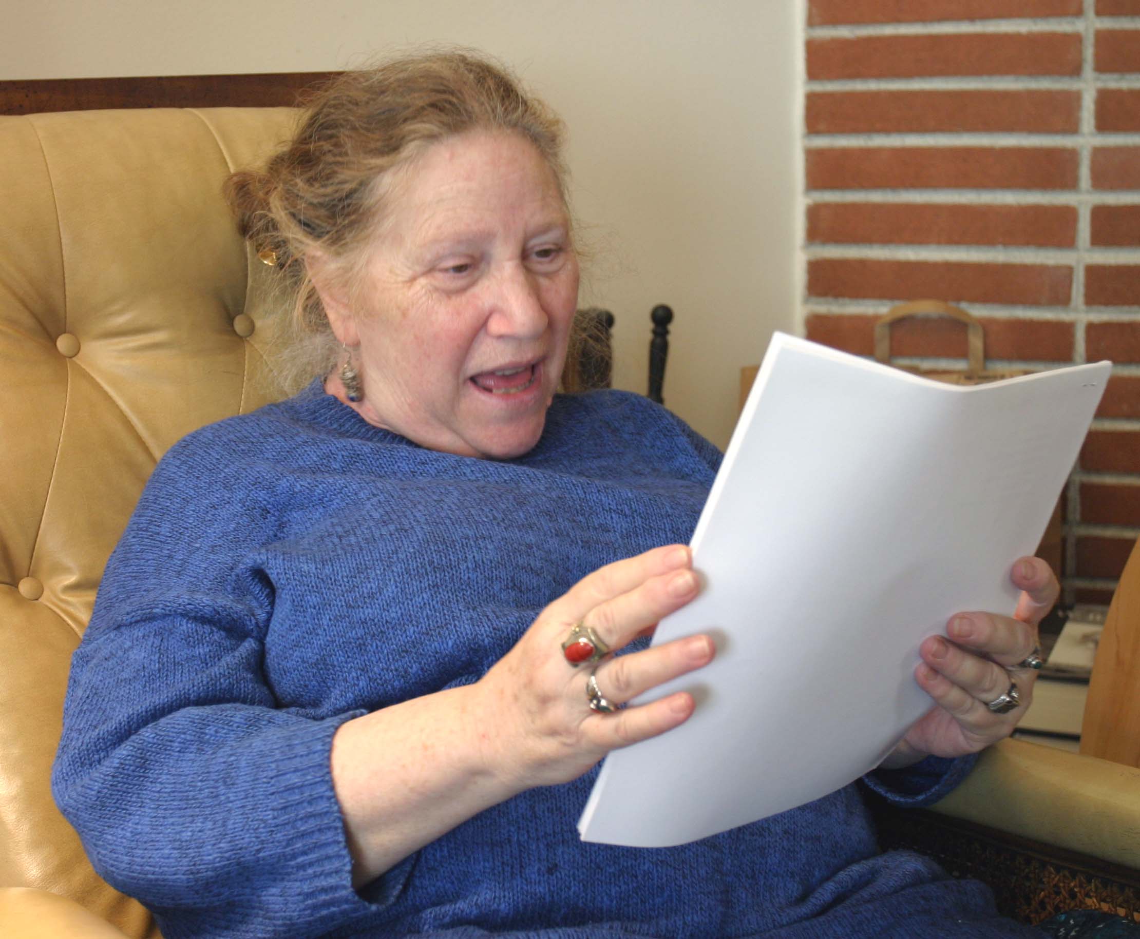 Diane di Prima legge alcuni fogli seduta in poltrona durante la registrazione di Add-Verse nel 2004